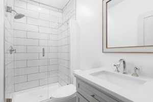 A white bathroom with a grey vanity cabinet, white marble countertop, and a shower with large rectangle tiles.