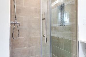 A modern shower with a stone floor, chrome fixtures, sliding glass door, and marble tiling on the walls.